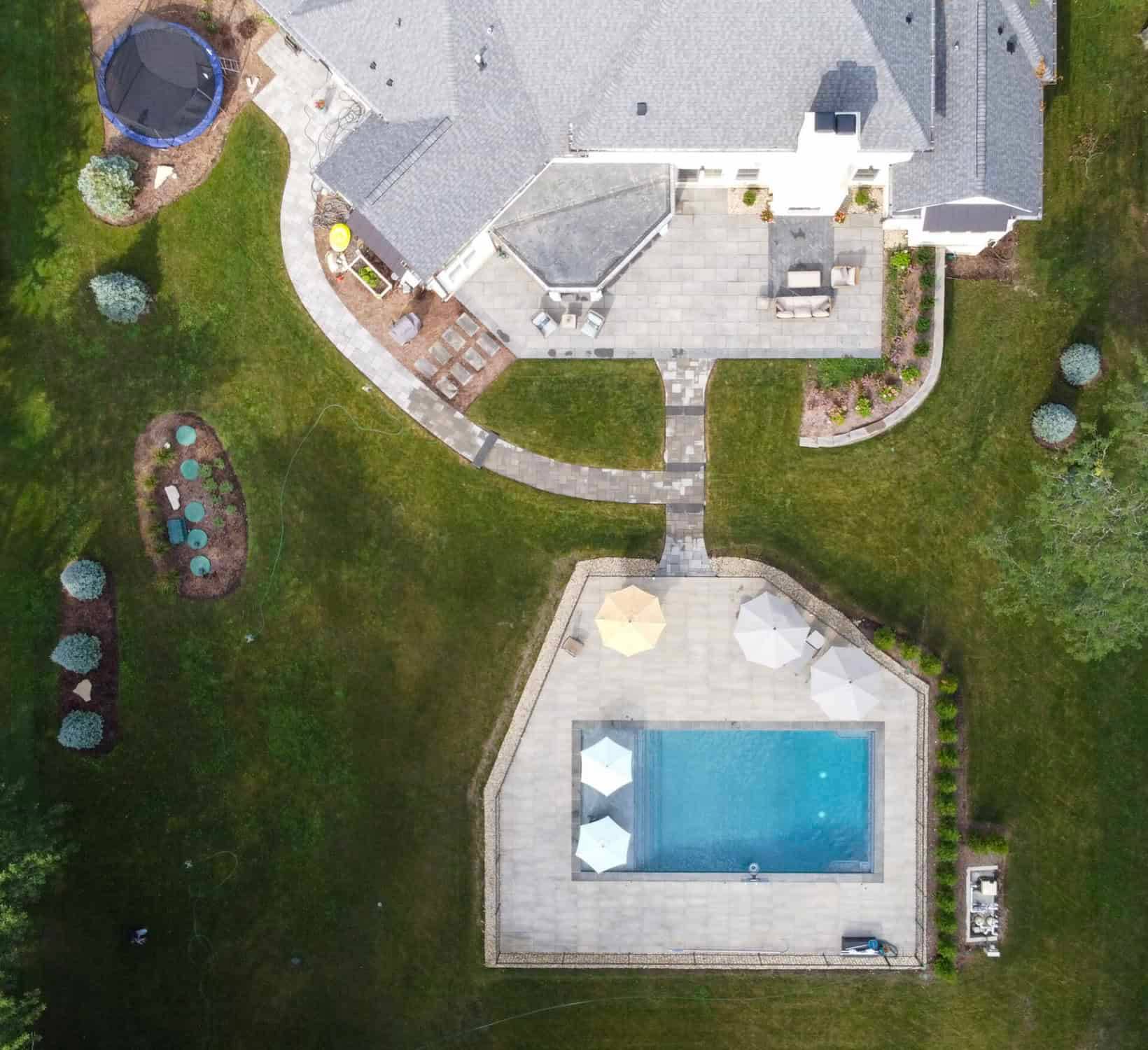 Aerial view of a completed rectangular pool, paver deck and fenced yard on a suburban property