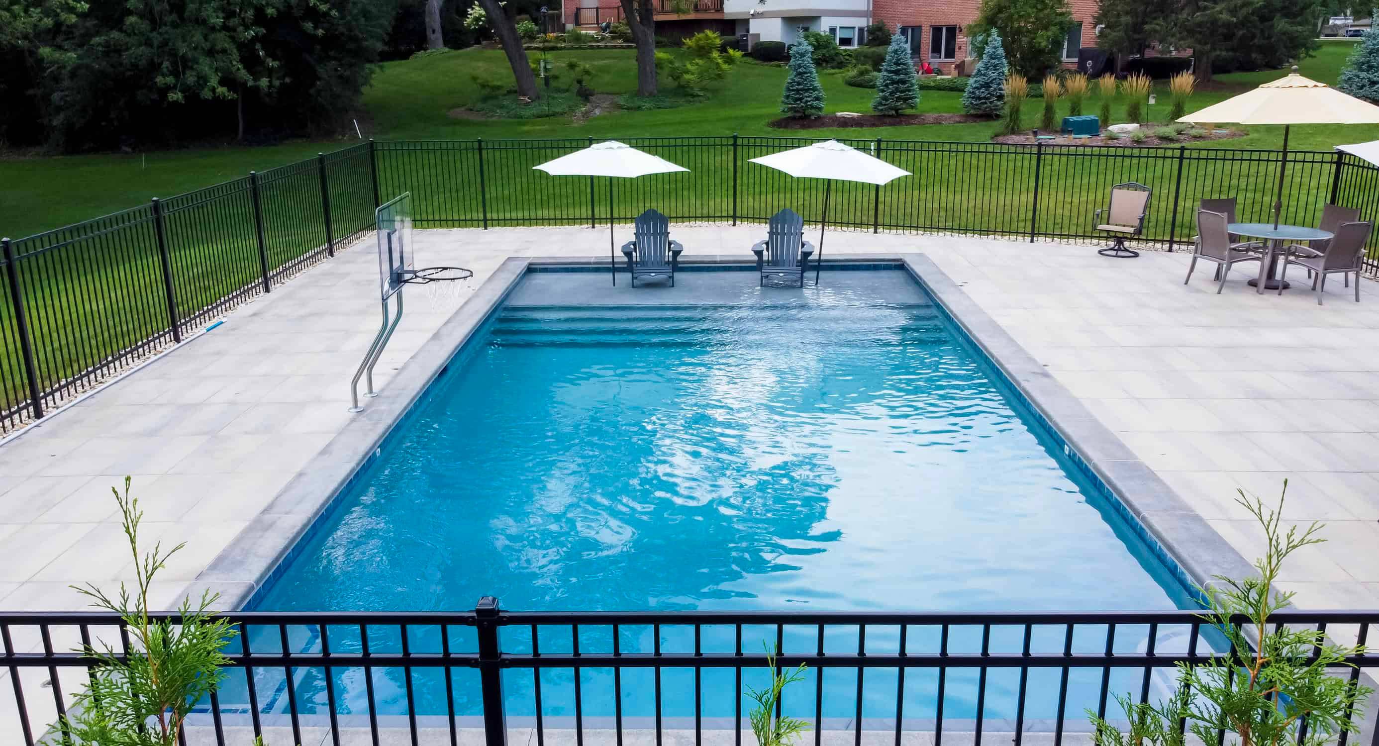Aerial view of a rectangular in-ground pool, fenced yard, and paver deck