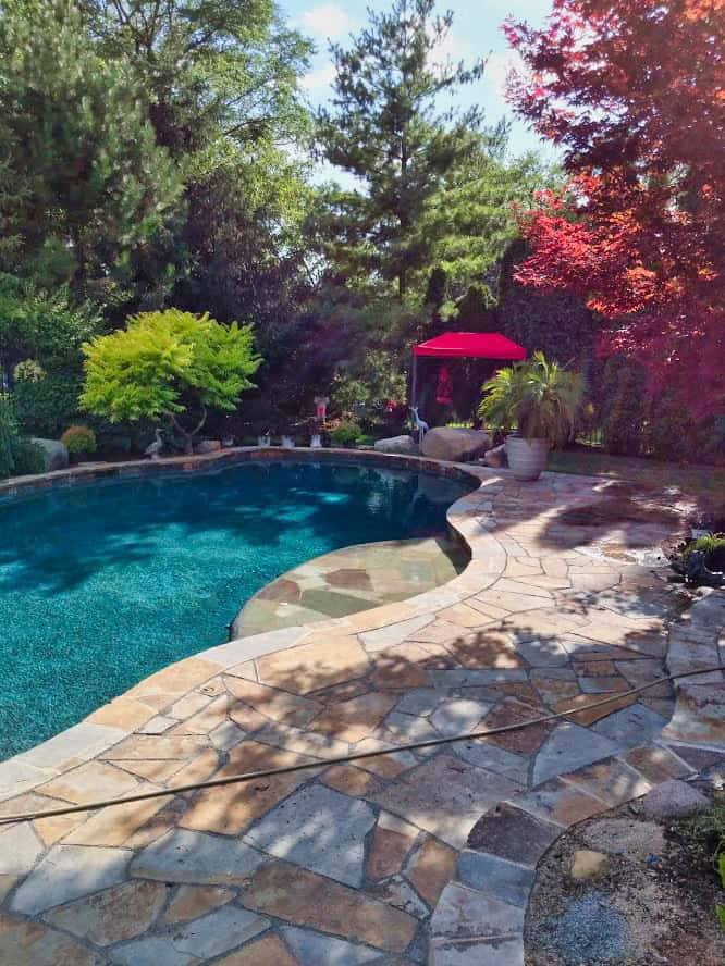 Freeform pool with a flagstone deck and a shade canopy in a compact backyard