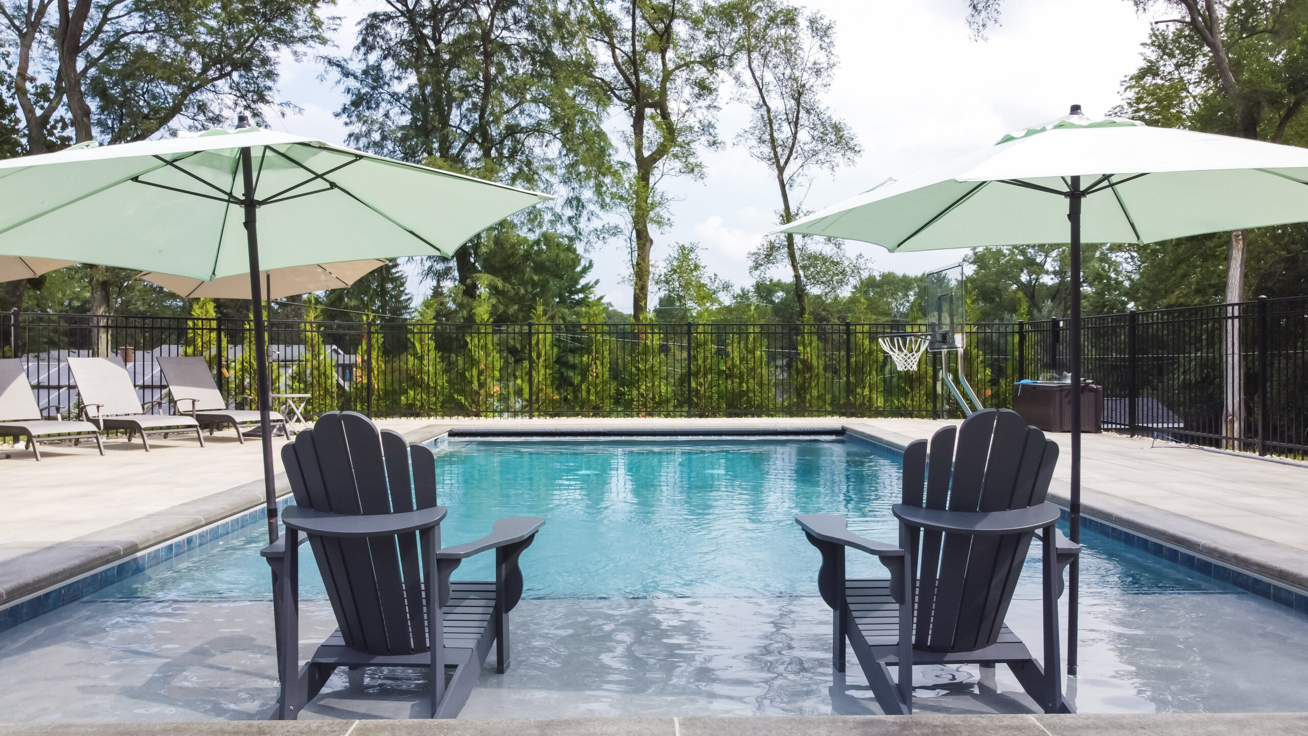 Rectangular in-ground pool with coping, a black aluminum fence, and stone patio