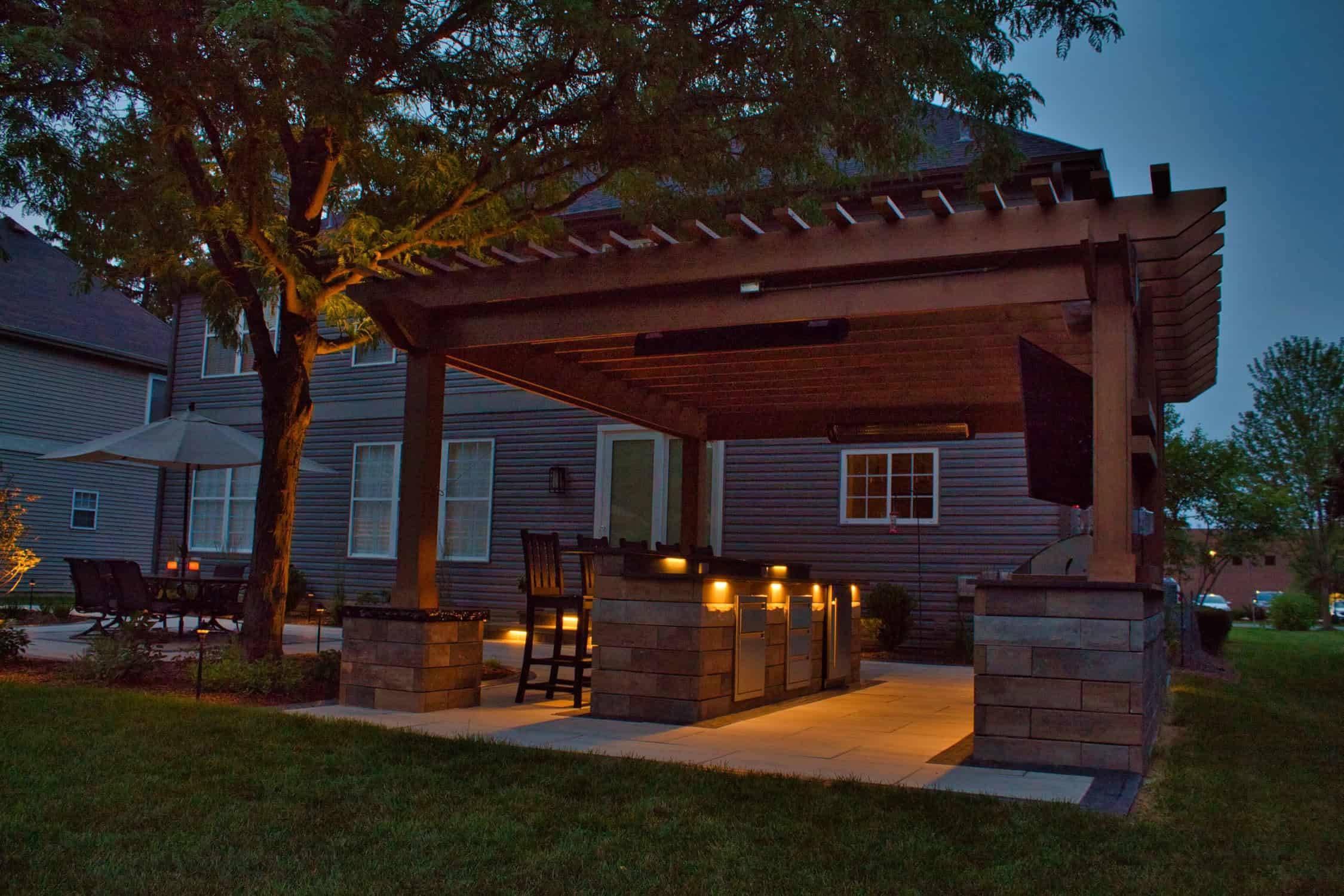 Cedar pergola and outdoor kitchen beside a lit bluestone patio at dusk