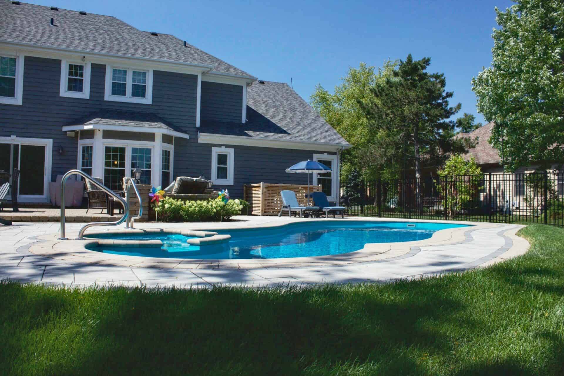 Completed freeform pool with a built-in bench and paver surround in a Chicago-area backyard