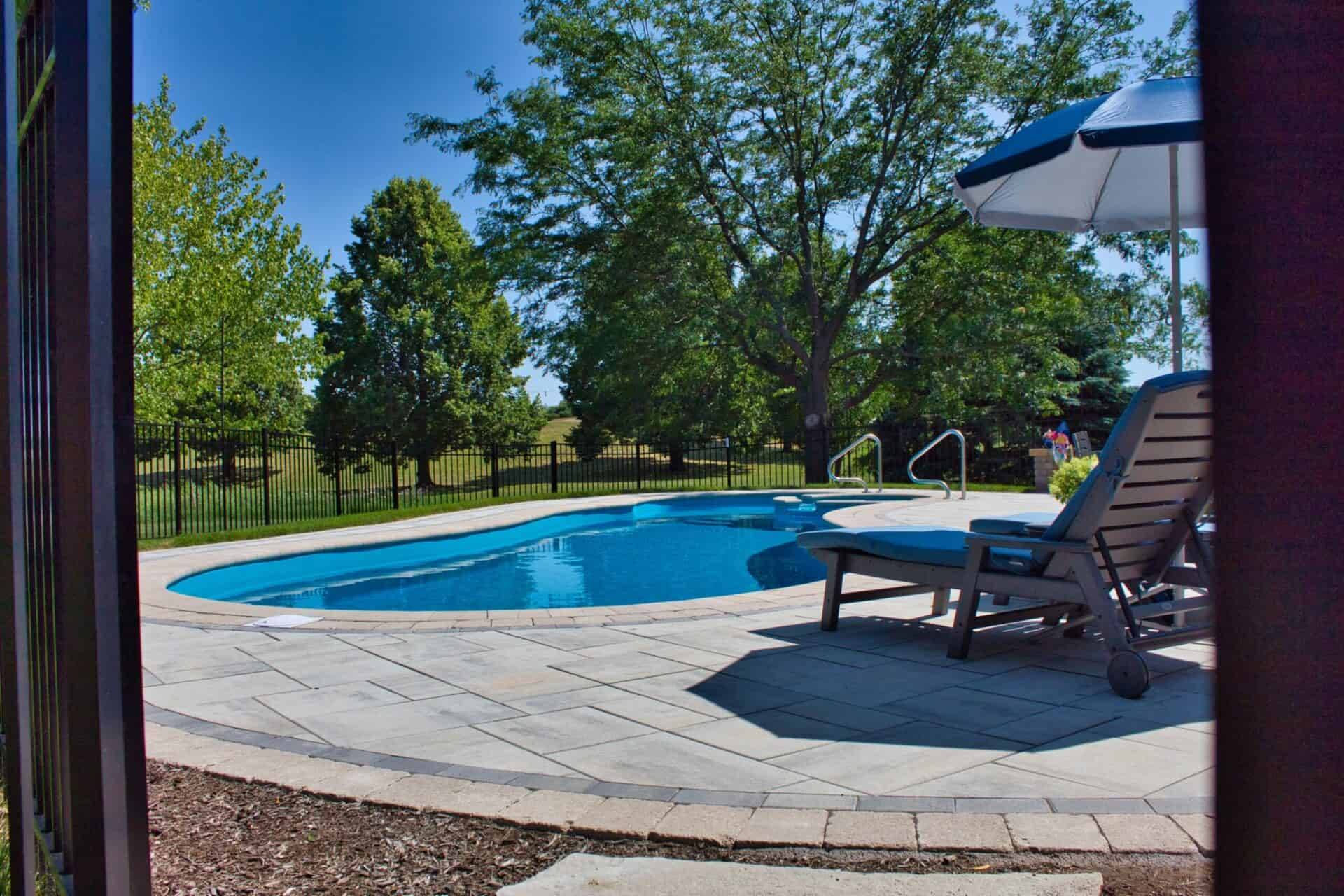 Freeform in-ground pool with a paver surround under a mature tree canopy