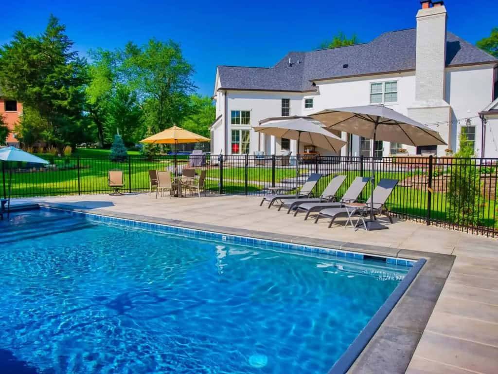 Rectangular in-ground pool with a paver deck, market umbrellas and lounge chairs behind a Chicago-area home